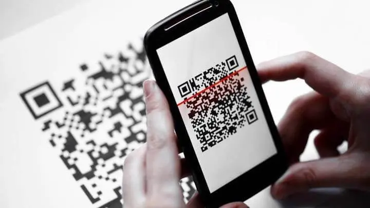 Hände halten ein Smartphone und scannen einen QR-Code auf einem Blatt Papier