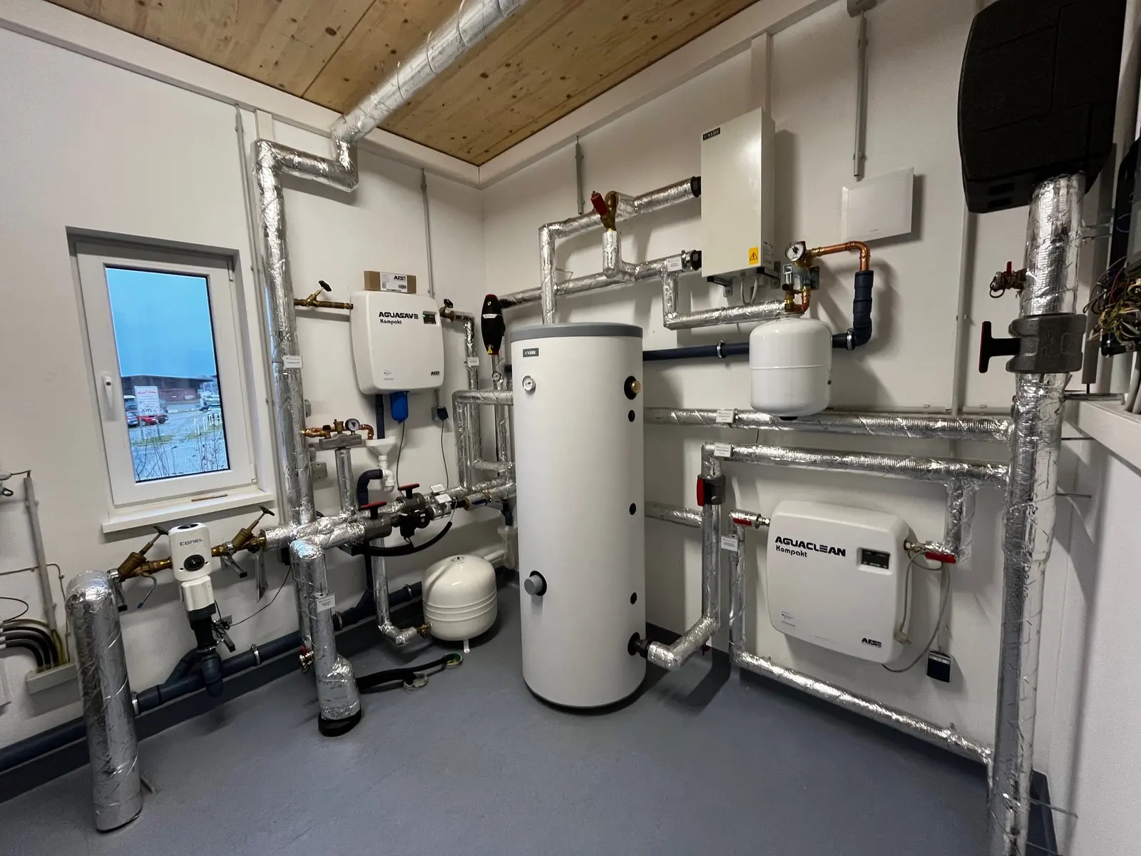 Technikraum des Neubaus mit Nibe-Warmwasserspeicher, gedämmten Rohrleitungen und Wandgeräten zur Wasseraufbereitung