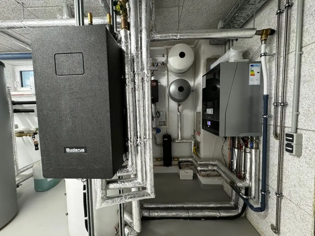 Wärmegedämmtes Buderus-Wärmepumpenmodul und wandhängendes Gas-Brennwertgerät im Heizungsraum des Mehrfamilienhauses