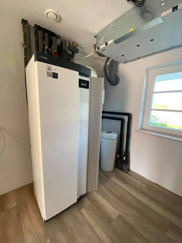Installierte weiße NIBE-Wärmepumpe in einem Technikraum mit Rohrleitungen und Lüftungsgerät unter der Decke