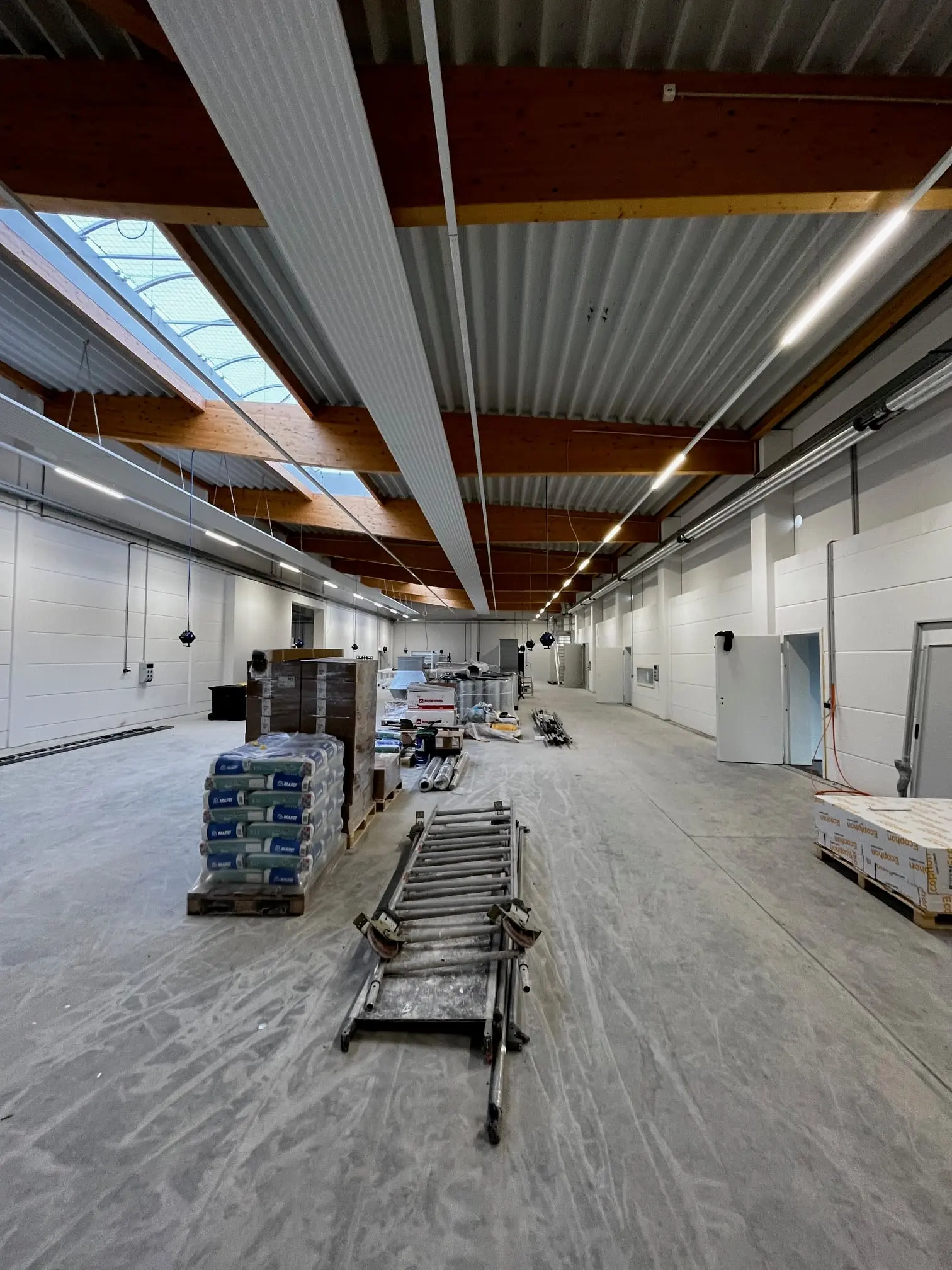 Betriebshalle der Tischlerei mit Holzträgern und Deckenbeleuchtung während der Installationsarbeiten
