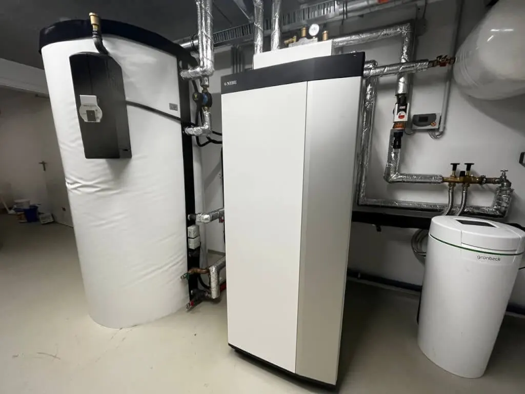 Technikraum des Neubaus mit vier Wohneinheiten: Wärmepumpe neben gedämmtem Speicher, angeschlossen über isolierte Rohrleitungen