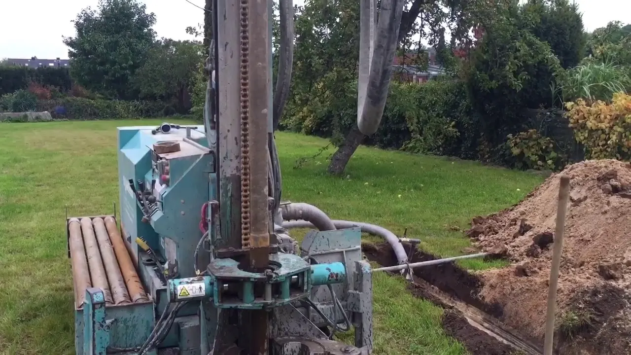 Bohrgerät im Garten eines Wohnhauses, daneben Bohrgestänge und der Aushub der Leitungsgrabens